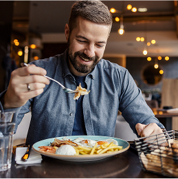 A man smiles while holding a fork with food on it