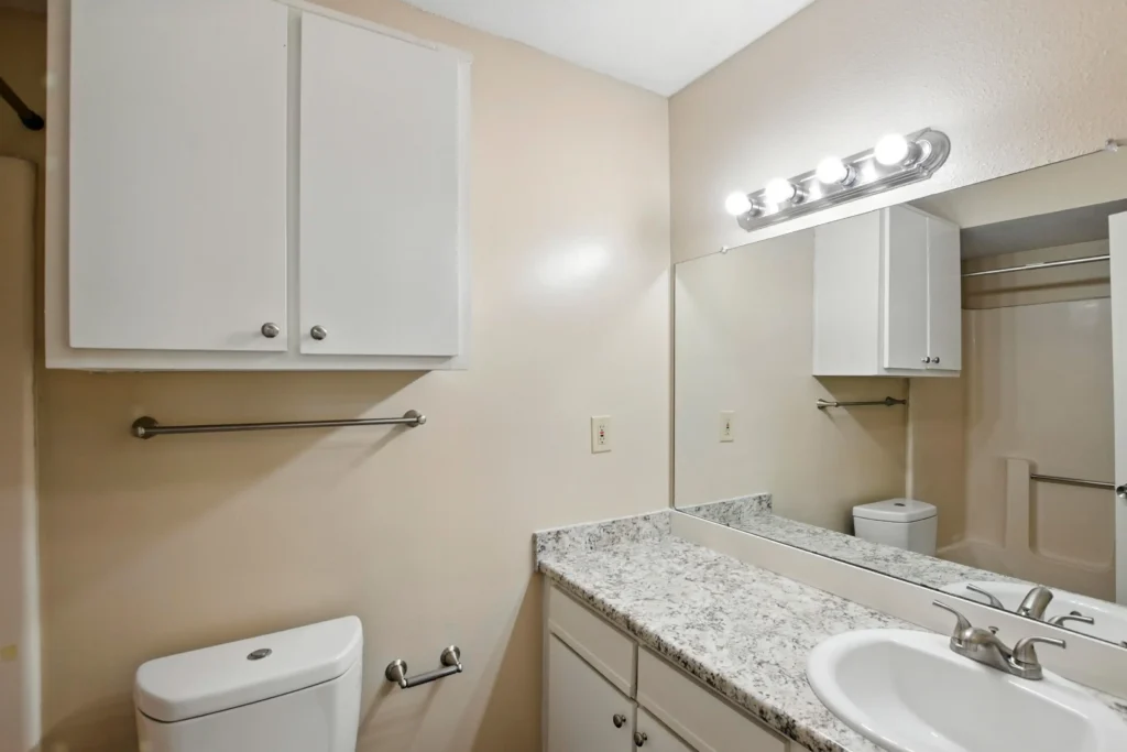 A bathroom with marble countertops and white cabinetry