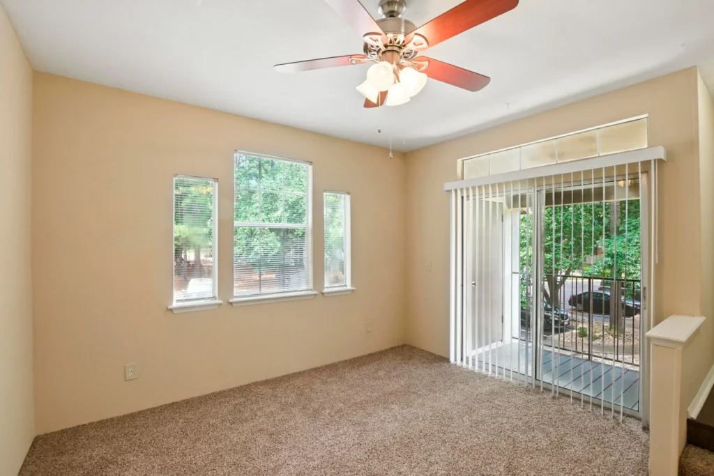 A carpeted bedroom with a ceiling fan and a sliding glass door leading to an outdoor balcony